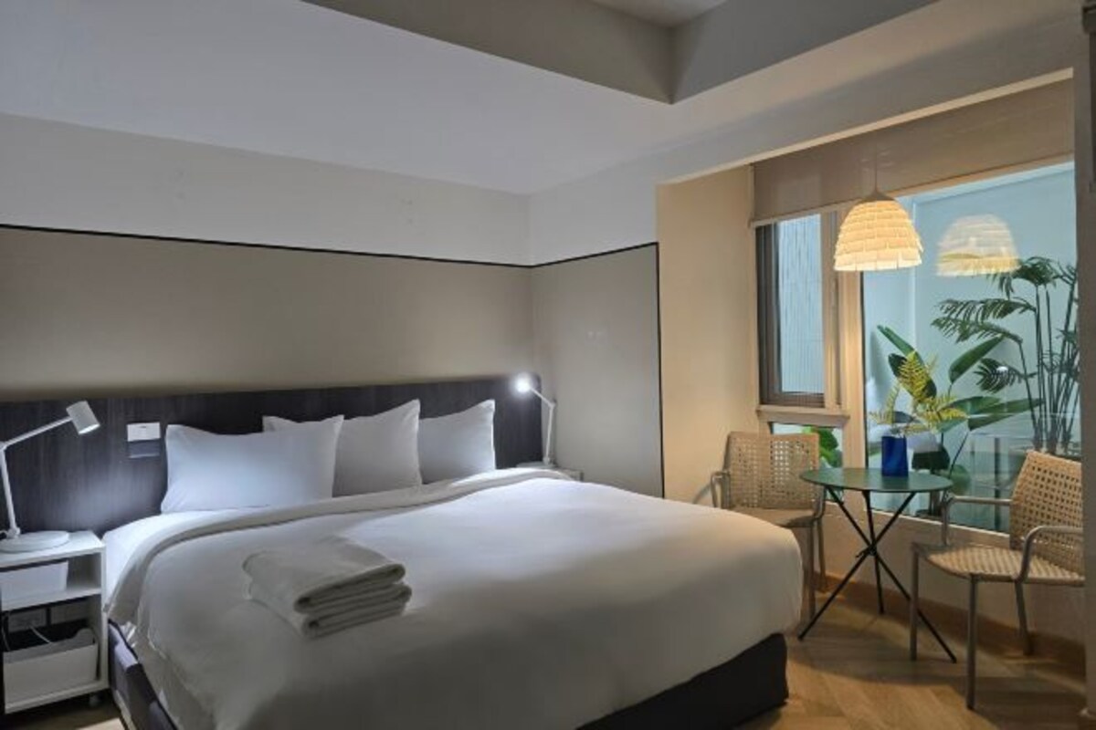 A hotel room with a large bed, bedside tables, a desk, and a balcony with chairs and plants.