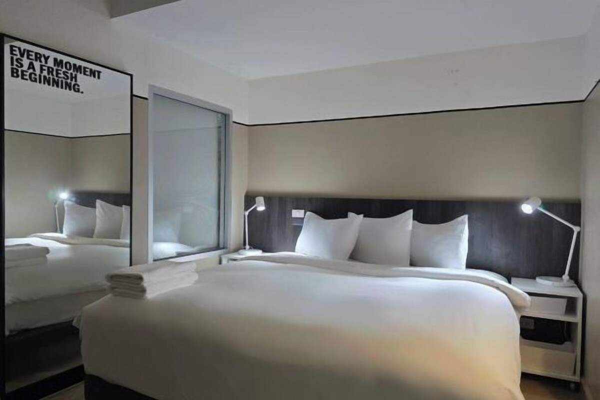 Una habitación de hotel moderna con una cama grande, mesitas de noche y un espejo.