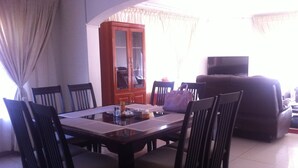 A dining area with a wooden table and chairs, a cabinet, and a television in the background. - Upper Room Guest House (Francistown)