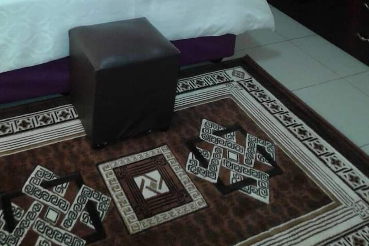 A neatly made bed with a white and orange bedspread, a small black ottoman, and a patterned rug.