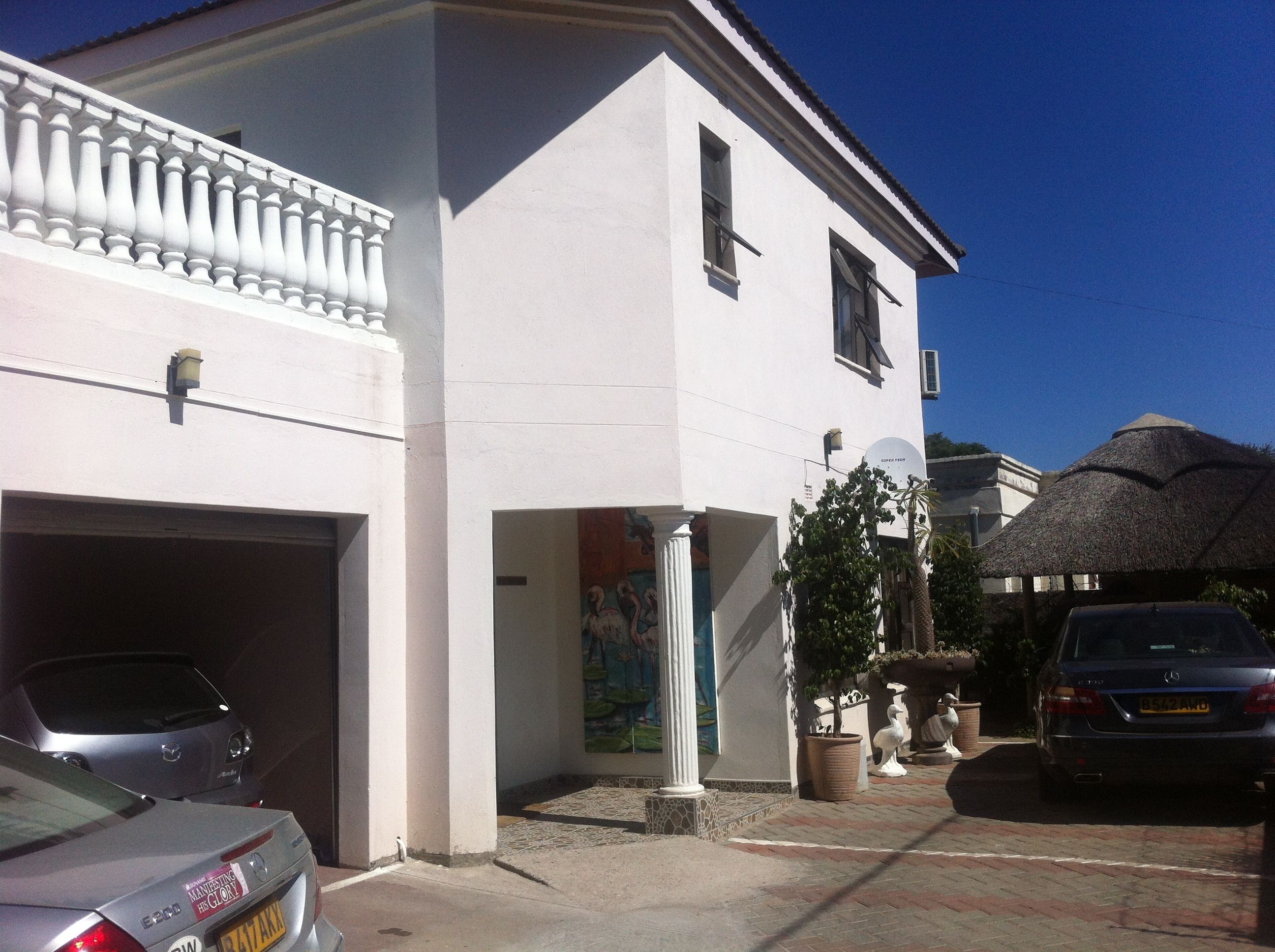 Ein weißes Gebäude mit Garage, einem strohgedeckten Anbau und einem geparkten Auto davor.