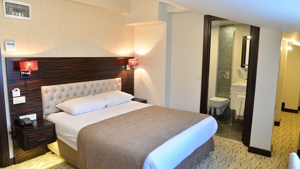 A hotel room with a large bed, a nightstand with a phone, and a bathroom visible through an open door. - Golden Siyav Hotel (Istanbul)