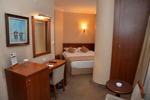 A hotel room with a bed, a desk with a chair, a small table, a mirror, and a wall-mounted light. - Golden Siyav Hotel (Istanbul)