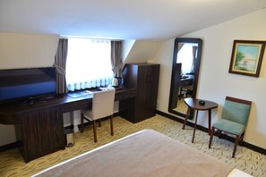 A hotel room with a bed, a desk with a chair, a small table, a wardrobe, a mirror, and a painting on the wall. - Golden Siyav Hotel (Istanbul)