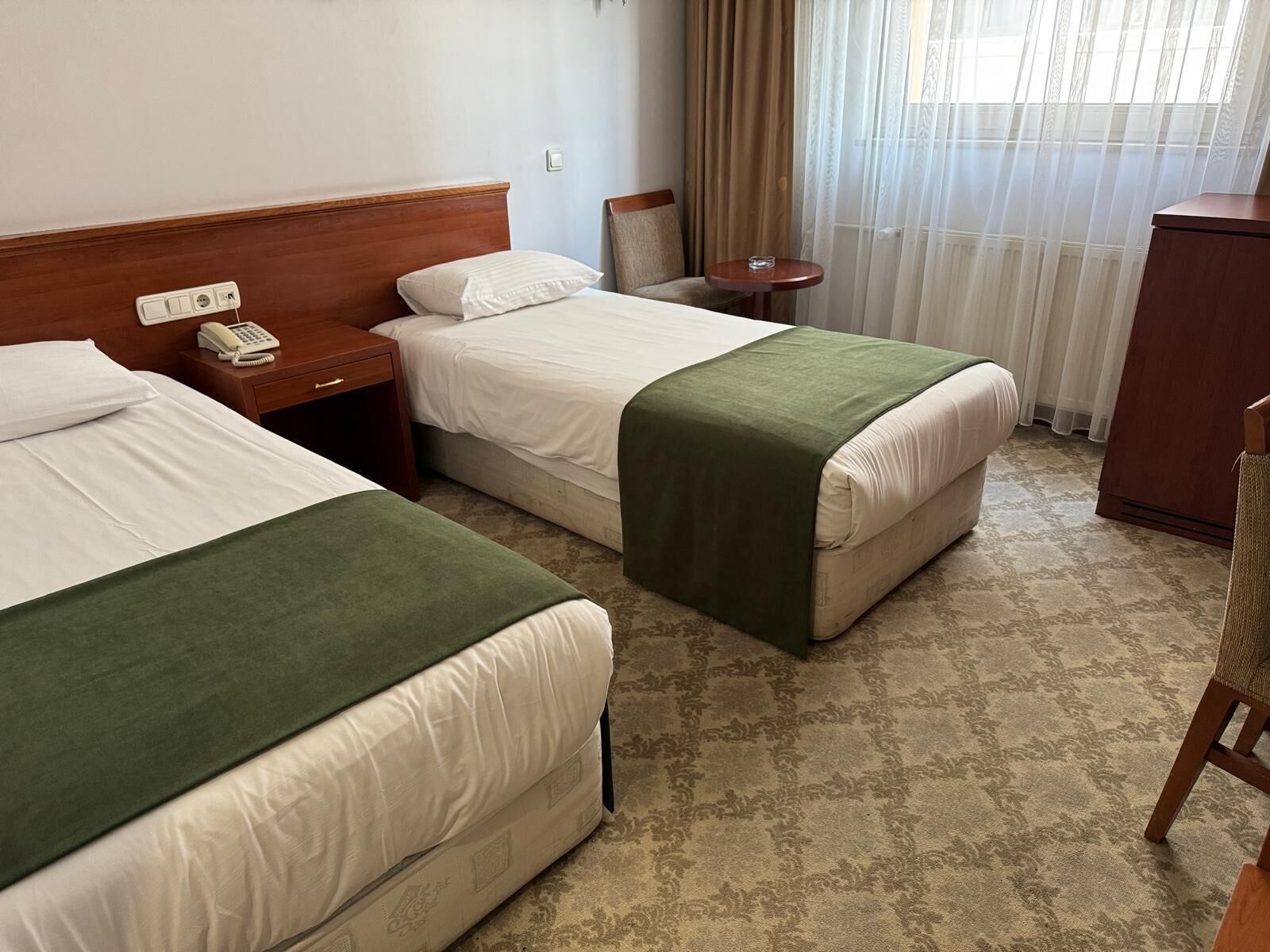 Camera d'albergo con due letti, una testiera in legno, un comodino con un telefono, un tavolino con un bicchiere e uno specchio.