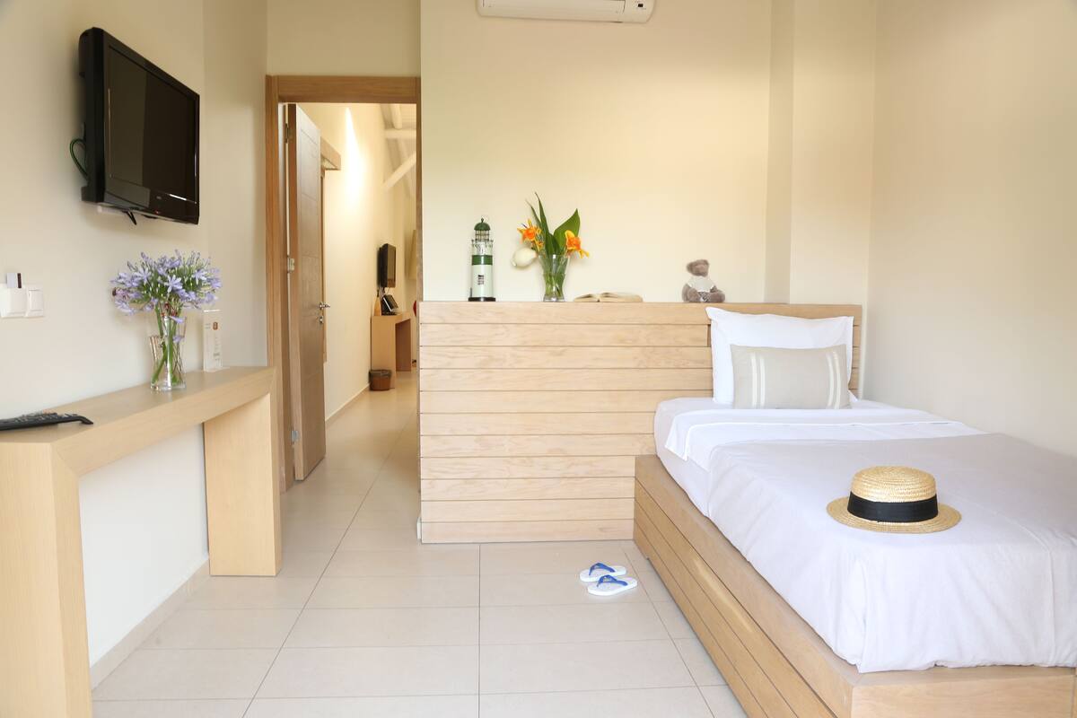 Une chambre d’hôtel avec un lit en bois, un téléviseur fixé au mur, un bureau agrémenté d’un vase de fleurs et une table de chevet.
