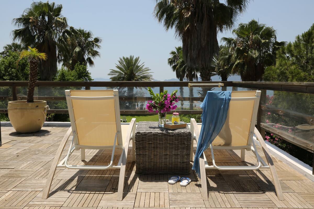 Un balcon avec deux chaises, une table en osier ornée d’un vase de fleurs et une plante en pot.