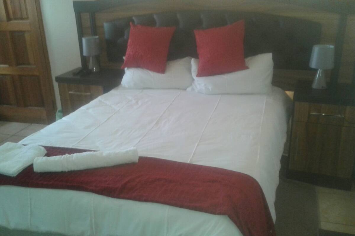 A neatly made bed with white and red bedding, two nightstands with lamps, and a wooden door in the background.