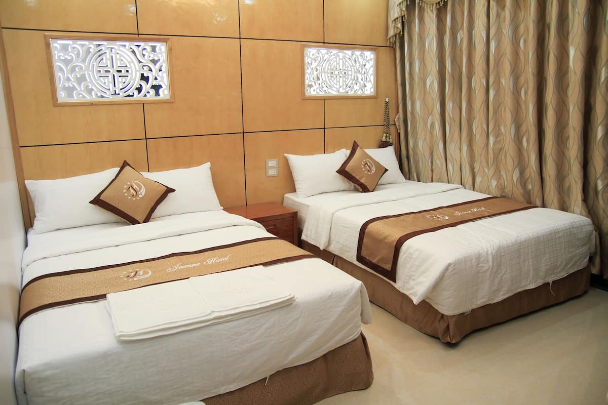 Two adjacent hotel beds with white linens, brown headboards, and decorative wall panels.
