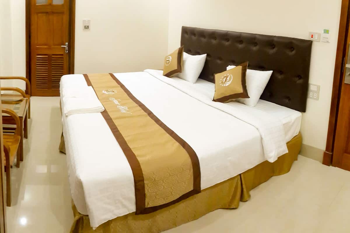 A hotel room with a large bed, a wooden chair, and a small table.