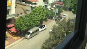 Une vue de rue avec des immeubles, des voitures garées et des arbres.