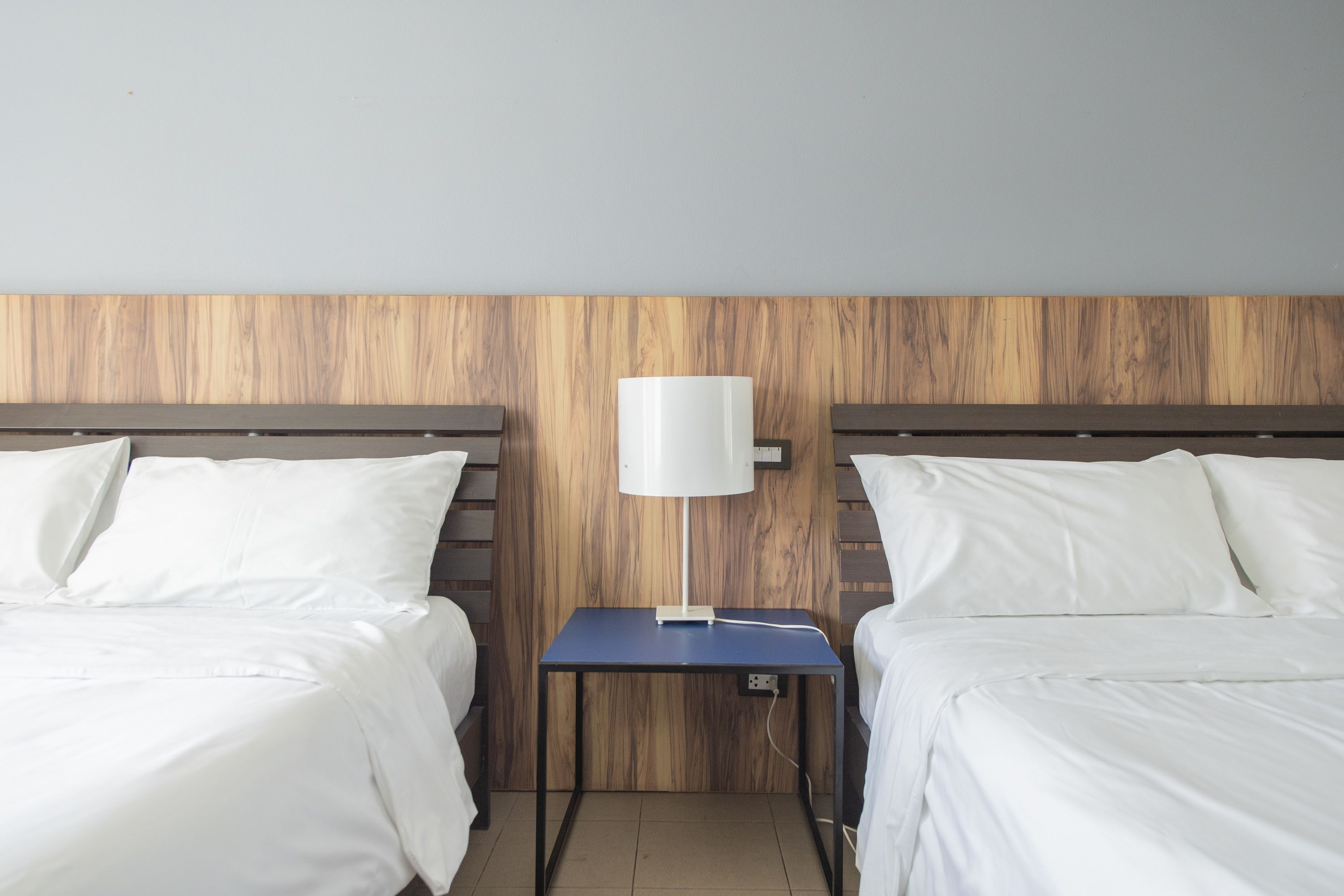 A hotel room with two beds, a small table with a lamp, and a wooden headboard.
