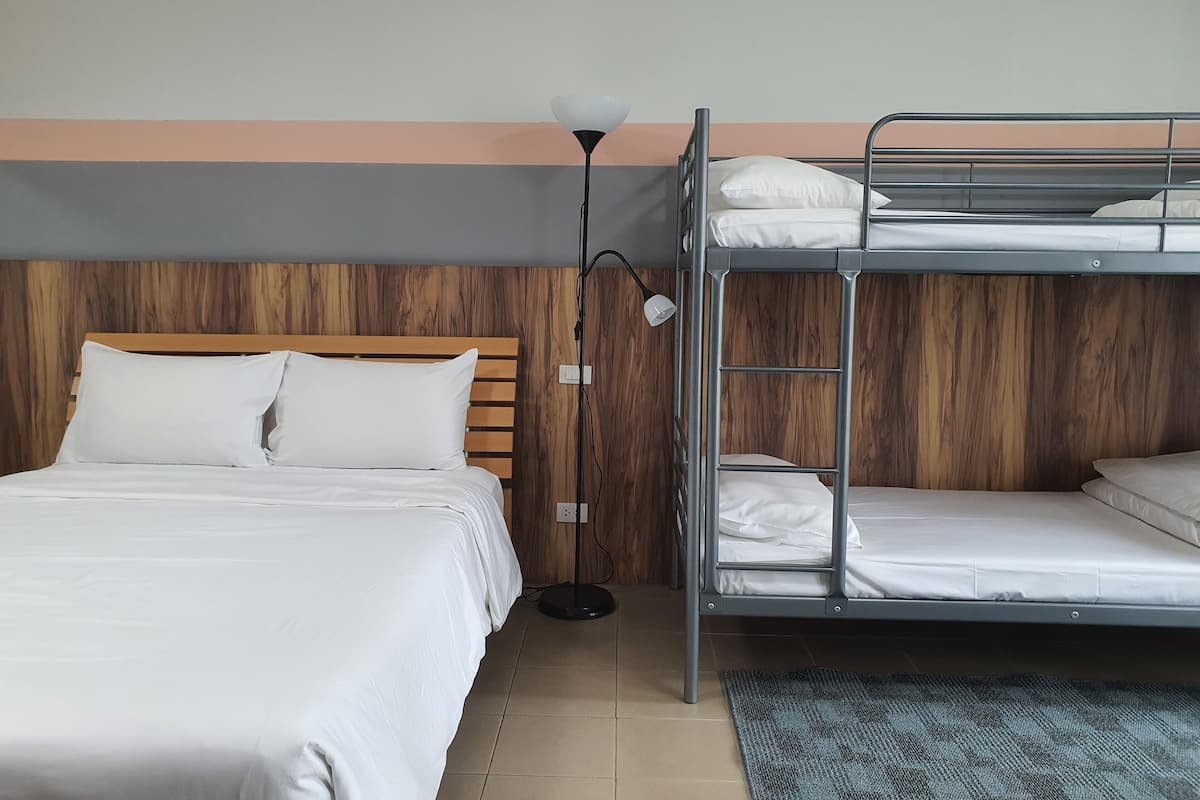 A room with a single bed, a bunk bed, a wooden headboard, a floor lamp, and a patterned rug.