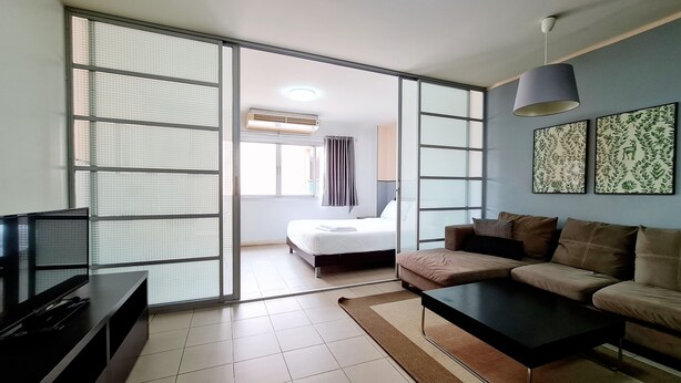 A modern hotel room with a bed, a sofa, a TV, and a sliding glass door leading to a balcony. - Sathorn Terrace Apartment (Bangkok)