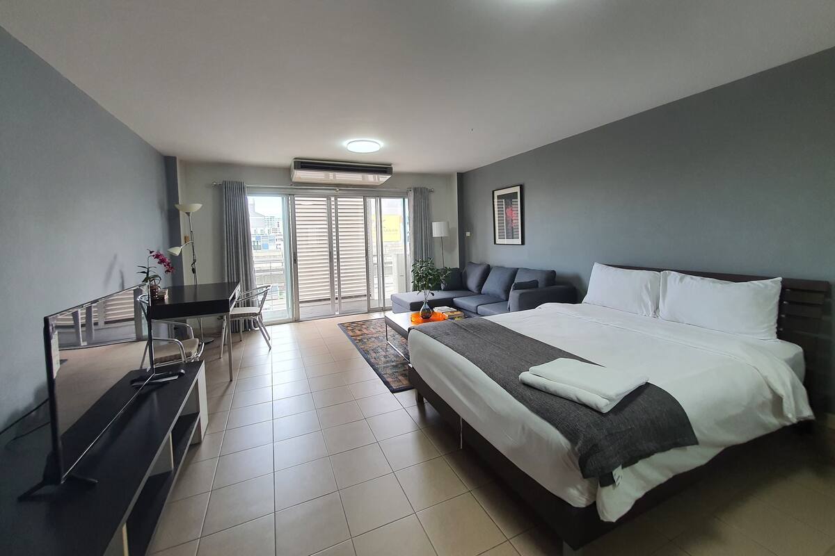 A modern hotel room with a large bed, a desk, and a balcony with sliding doors.