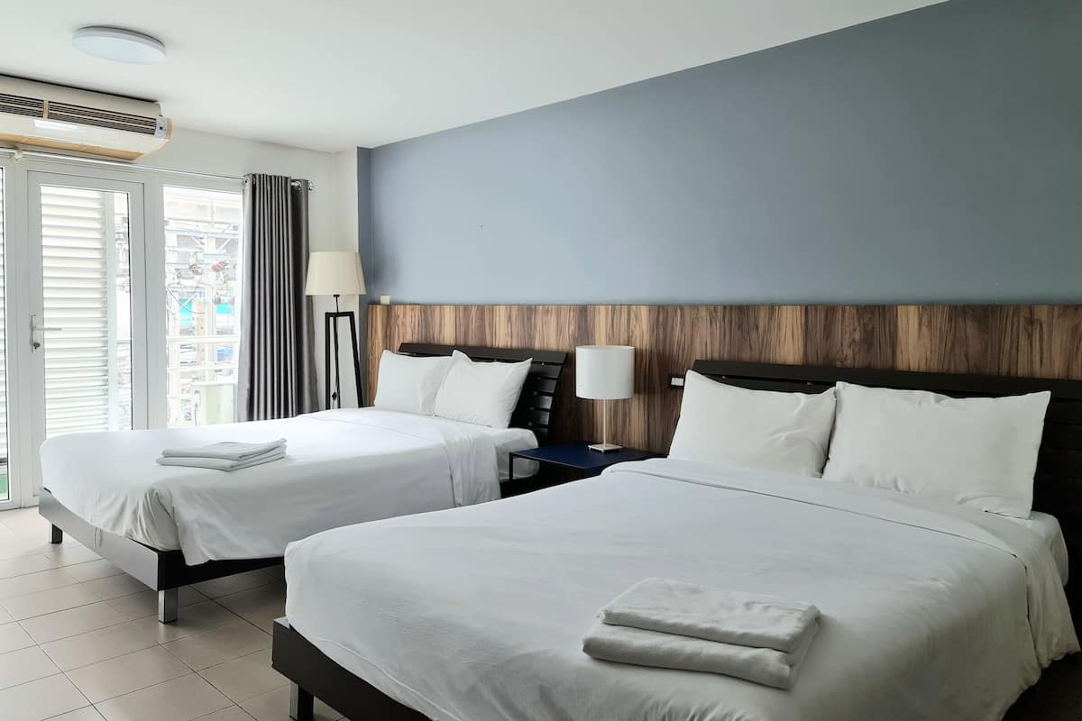 A hotel room with two beds, a ceiling fan, a nightstand with a lamp, and a view of the outside.