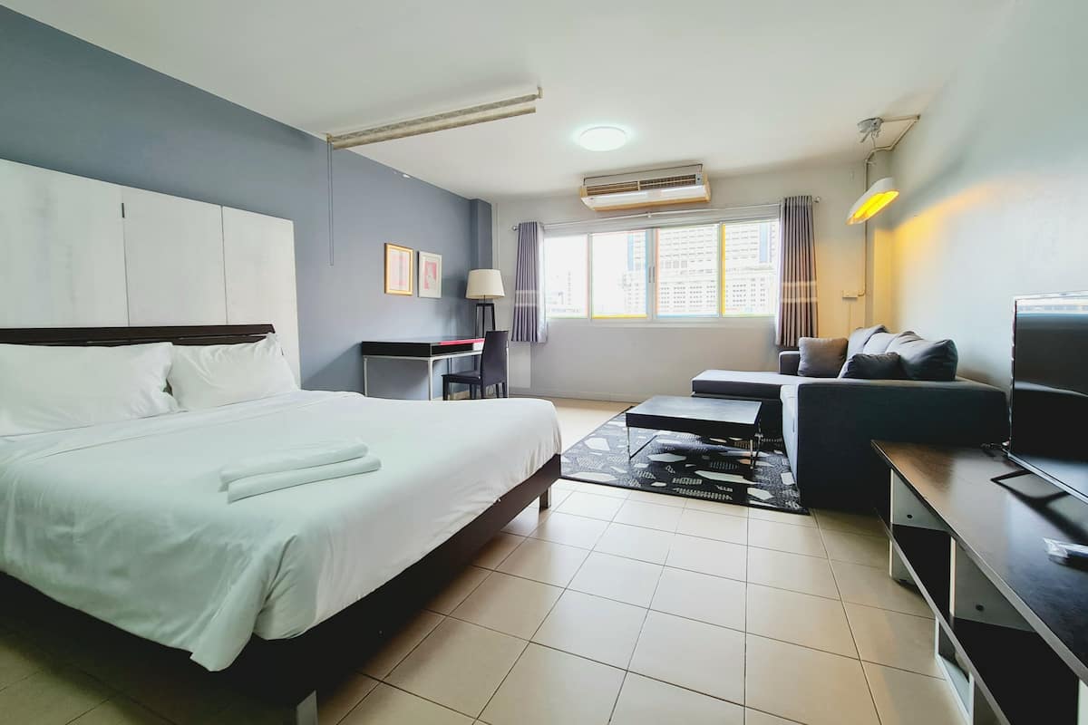 A hotel room with a bed, a desk, a sofa, a TV, and a window with curtains.