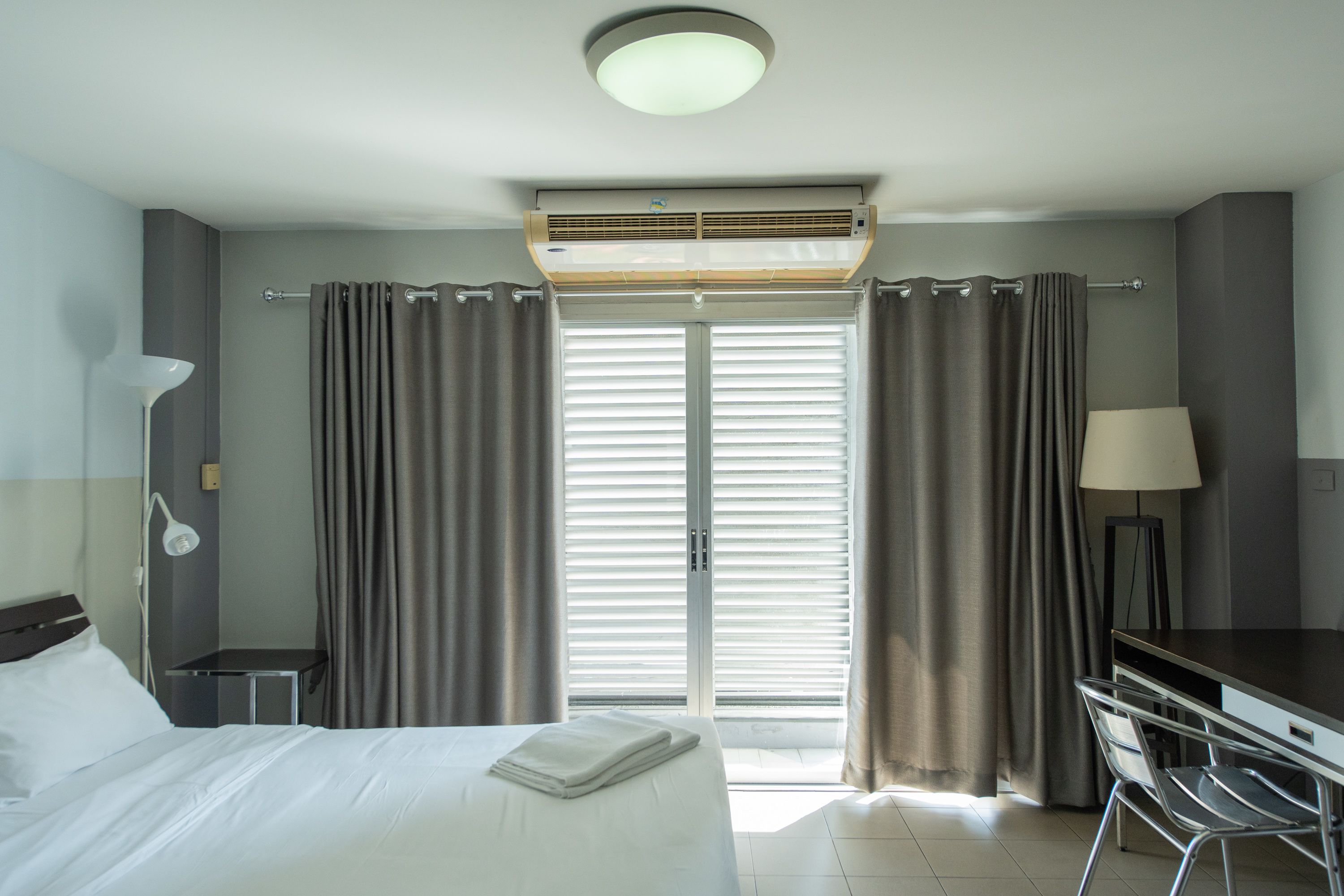 Une chambre d’hôtel avec un lit, un bureau, une lampe et un ventilateur de plafond.