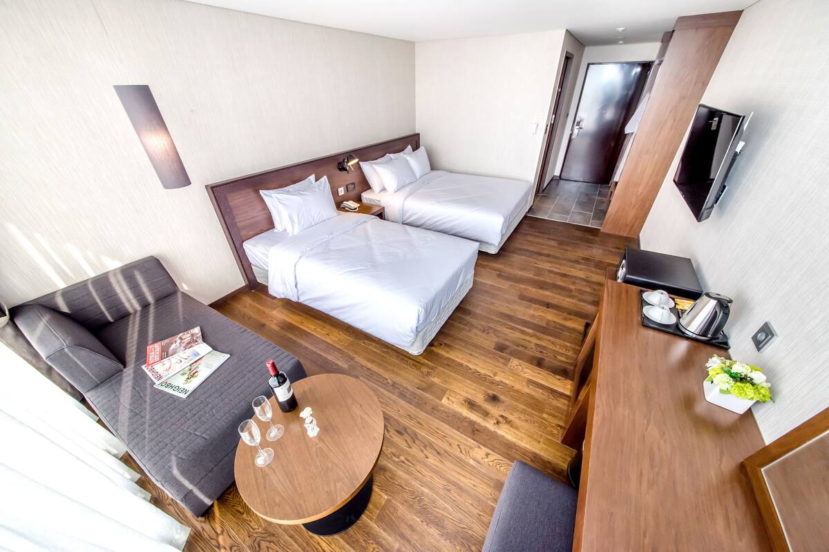 A hotel room with two beds, a sofa, a coffee table, and a TV.