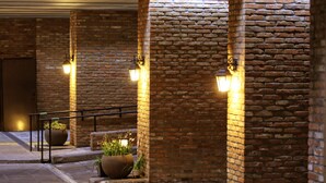 A brick corridor with a metal railing, potted plants, and wall-mounted lights. - Odri Inn Jeju (Jeju City)