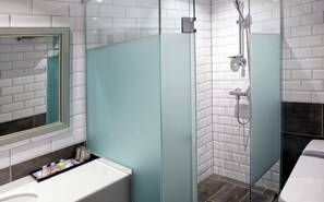 A modern bathroom with a glass shower enclosure, white tiled walls, and a white sink with toiletries.