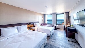 A hotel room with two beds, a small seating area, a desk, and a large window with a view of the sea. - Odri Inn Jeju (Jeju City)
