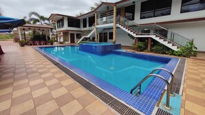 A swimming pool with a tiled deck, a covered seating area, and a staircase leading to a second floor.