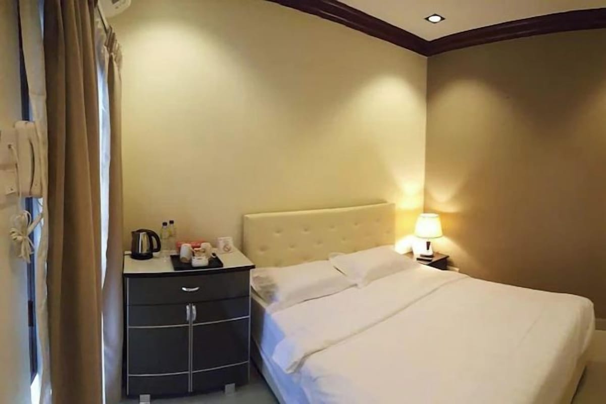 Una habitación de hotel con cama, mesita de noche, lámpara y armario.