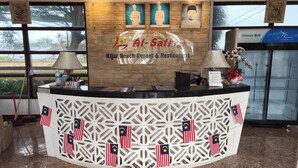 Un comptoir d’accueil à l’hôtel-restaurant Al-Safina Jual Beach Resort, orné de drapeaux malaisiens, de portraits encadrés et d’un logo.