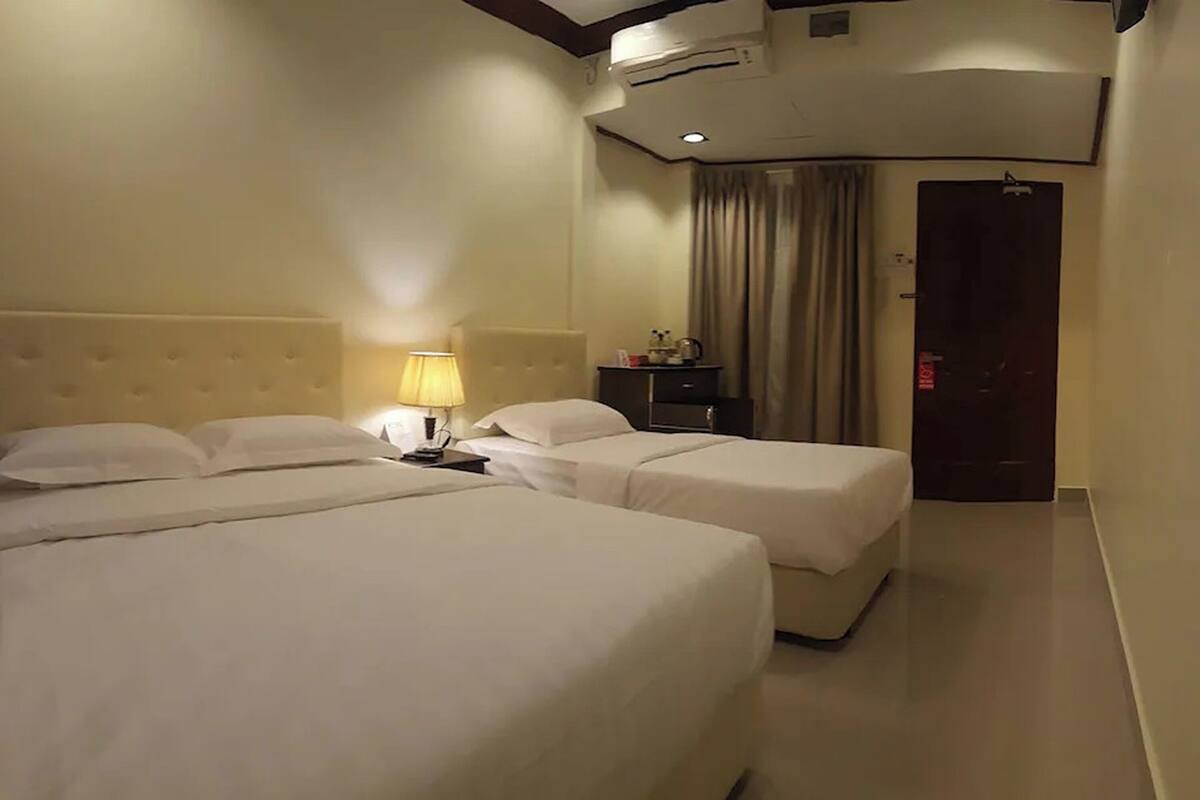 Een hotelkamer met twee bedden, een nachtkastje met lamp, een airconditioning en een deur met slot.