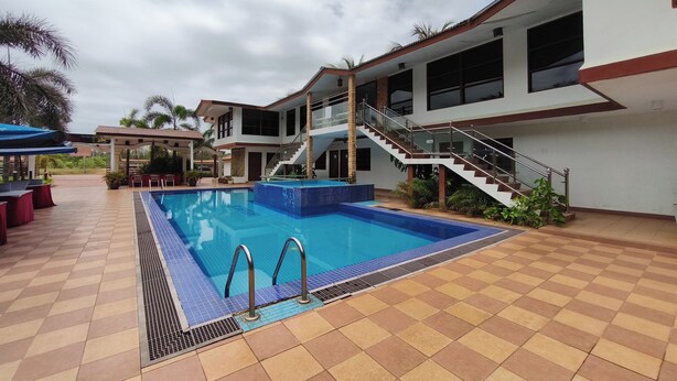 Une piscine avec une terrasse carrelée, un escalier et un espace couvert équipé de chaises.