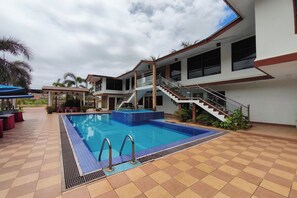 Ein Schwimmbecken mit Fliesenbord, einer Treppe und einem überdachten Bereich mit Stühlen.