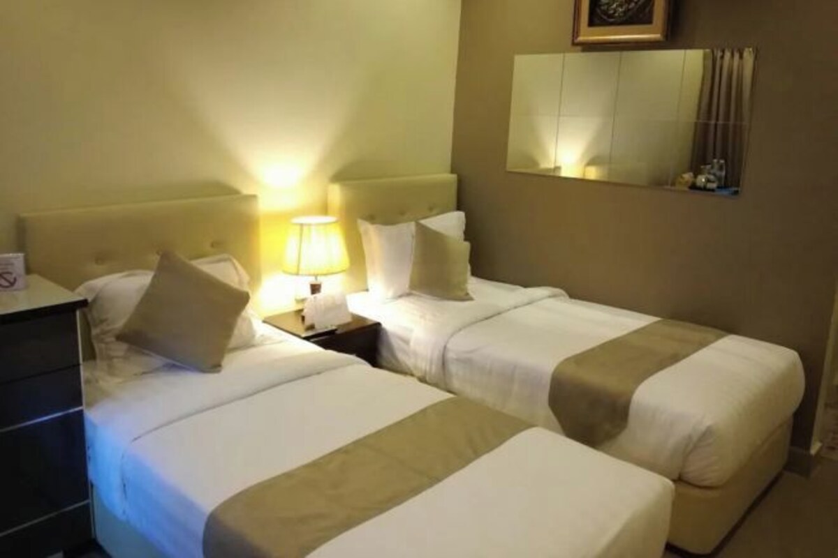 Una habitación de hotel con dos camas, una mesita de noche con lámpara, un aparador y un espejo en la pared.