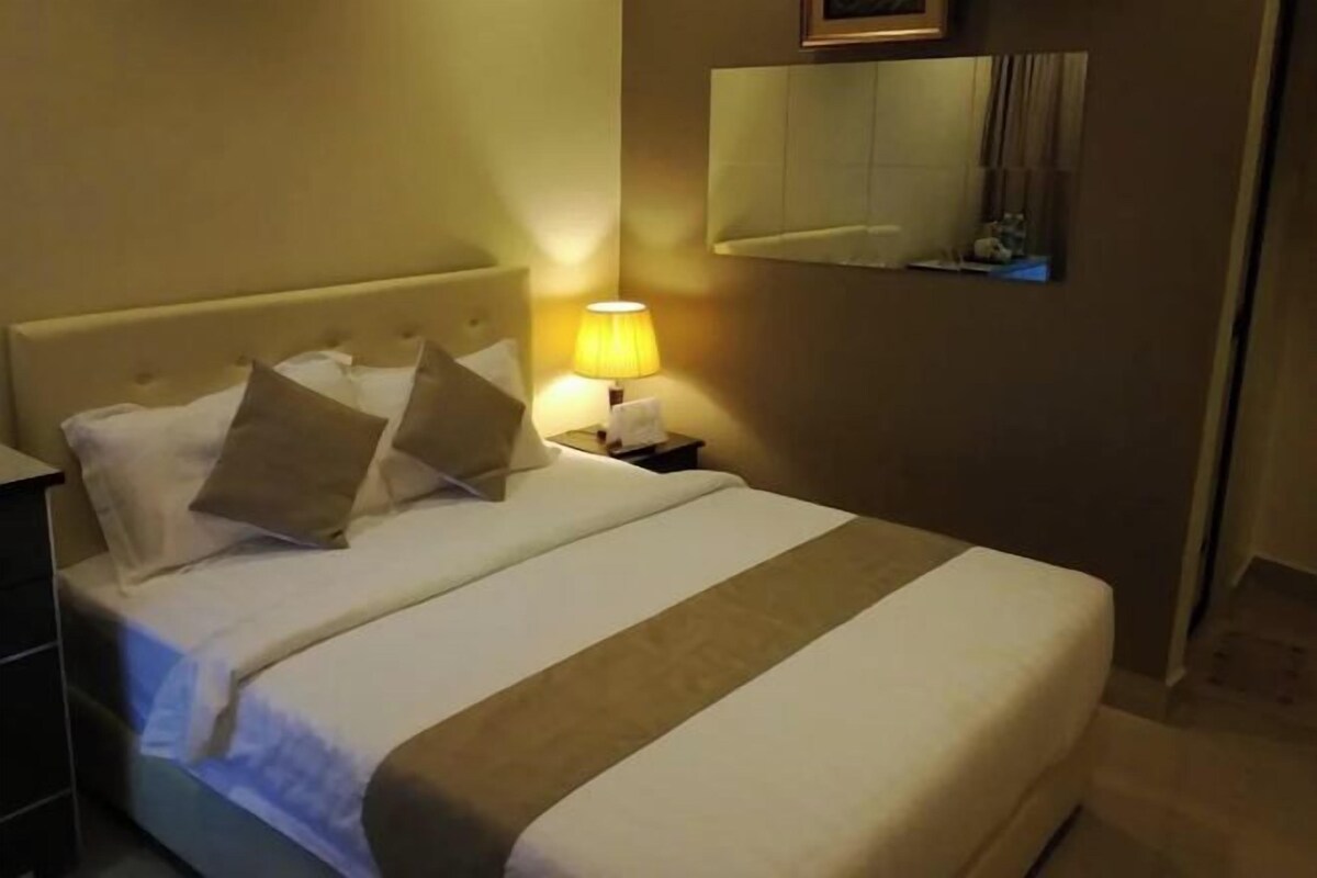 Ein Hotelzimmer mit einem Bett, einem Nachttisch mit Lampe, einem Spiegel an der Wand und einer Kommode.