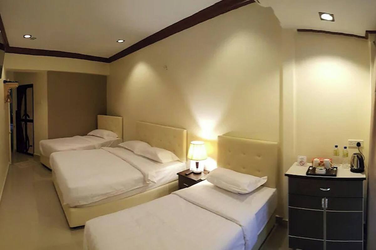 Een hotelkamer met drie bedden, een nachtkastje met een lamp en een minibar.