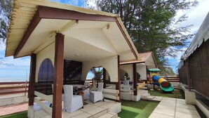 Un espace extérieur aménagé, abrité et doté de sièges, avec une piscine, un espace de jeux pour enfants avec un toboggan, et une vue sur la mer.