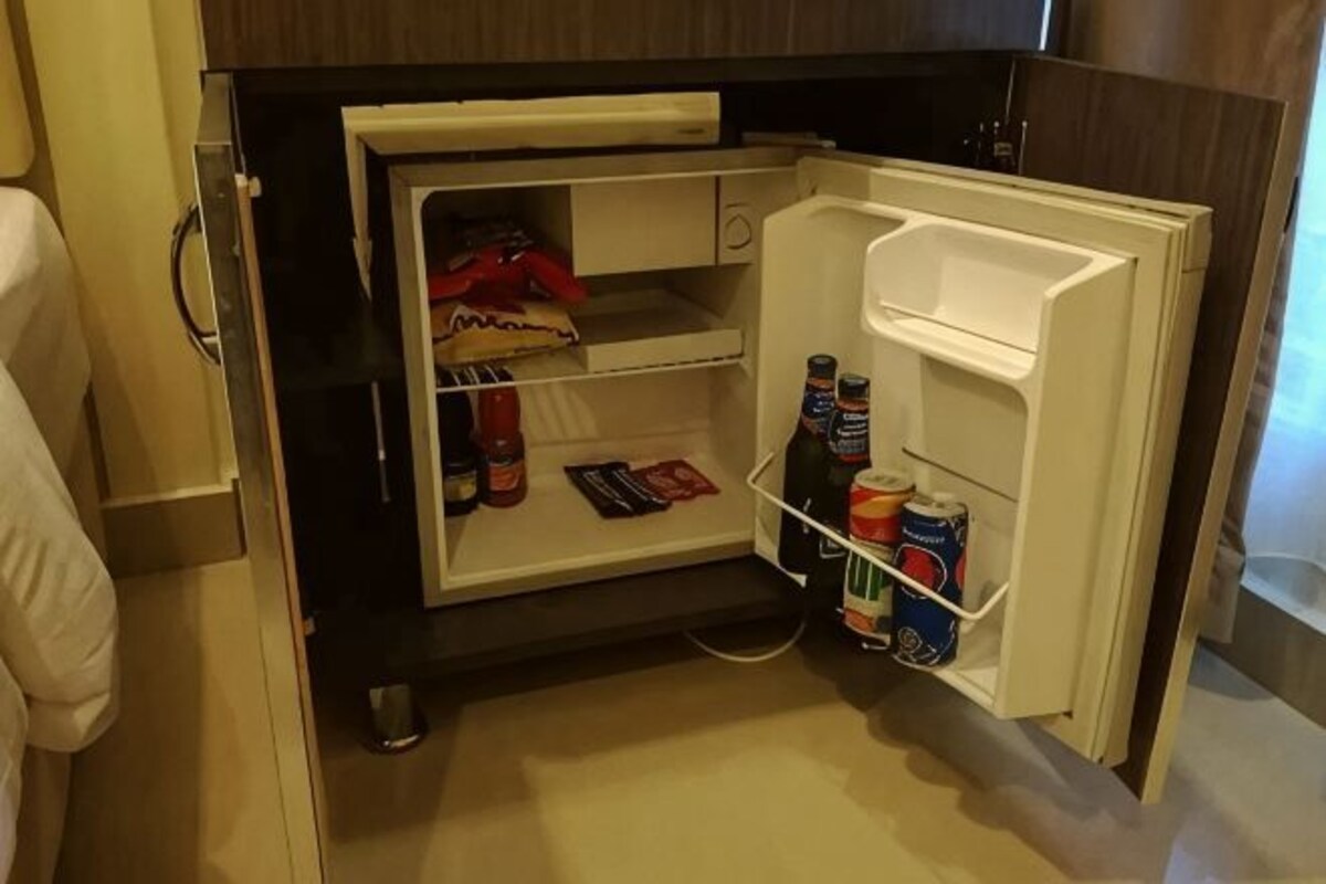 Un refrigerador compacto con un compartimento congelador, un estante pequeño y un repisa en la puerta con bebidas.