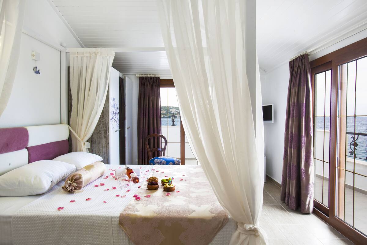 Une chambre d’hôtel avec un lit, un balcon avec des rideaux et une vue sur la mer.