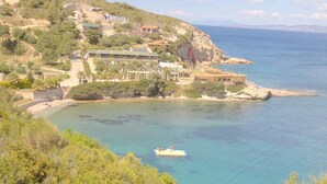 A coastal area with buildings on a hillside overlooking a calm sea. - Uzum Iskelesi Butik Otel (Karaburun)
