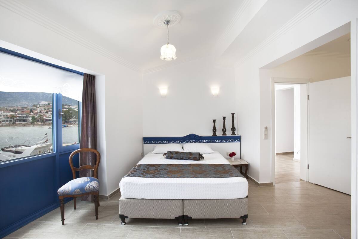 Une chambre avec une grande fenêtre, un lit, une chaise et une table de chevet.