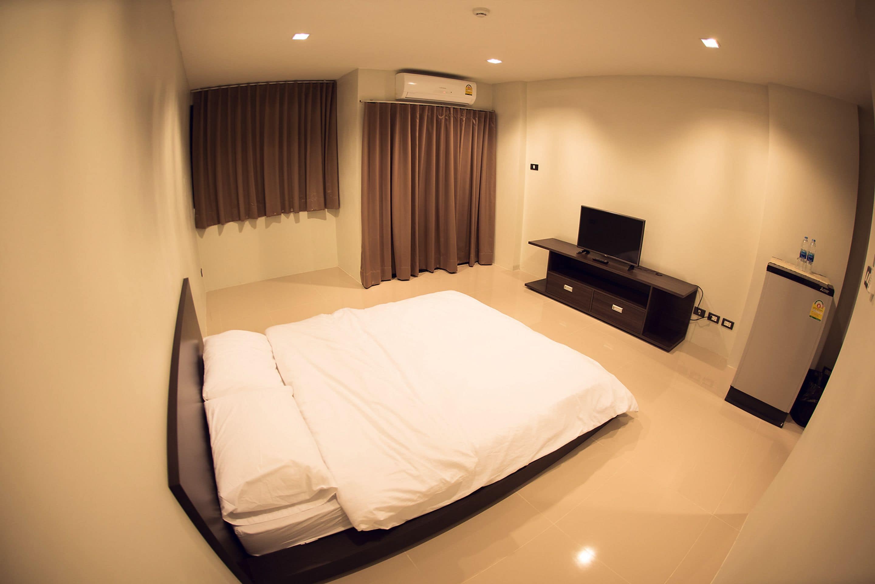 A hotel room with a bed, a TV, a minibar, and an air conditioning unit.