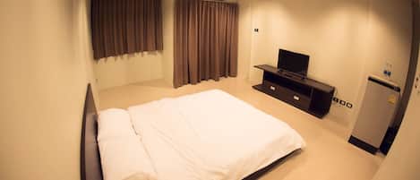 A hotel room with a bed, a TV, a minibar, and an air conditioning unit.