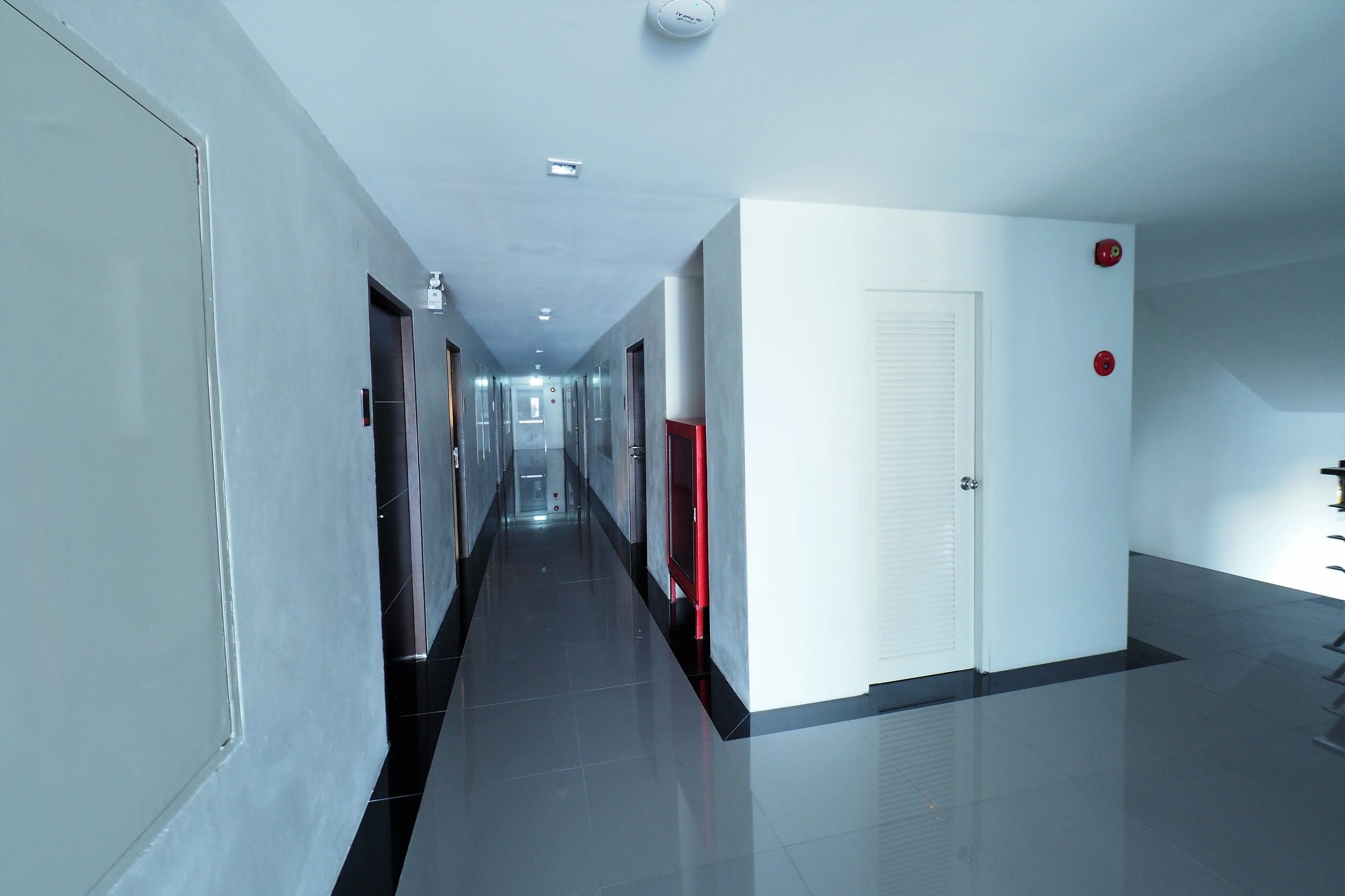 A modern, well-lit hallway with a long corridor, doors, and a red emergency exit sign.