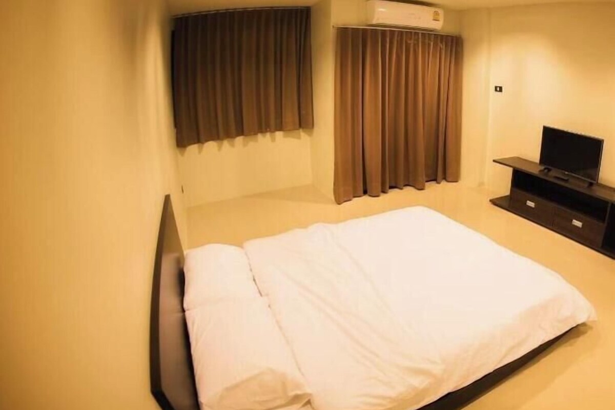 A hotel room with a bed, curtains, an air conditioning unit, and a TV stand.