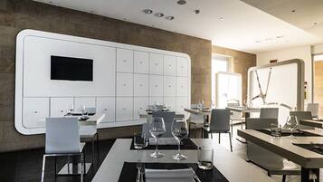 Un comedor moderno con mesas dispuestas para dos, equipadas con copas de vino y cubiertos.