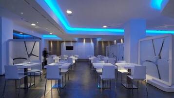 Um saguão de hotel moderno, com uma área de recepção central, mobiliário branco e iluminação ambiente azul.