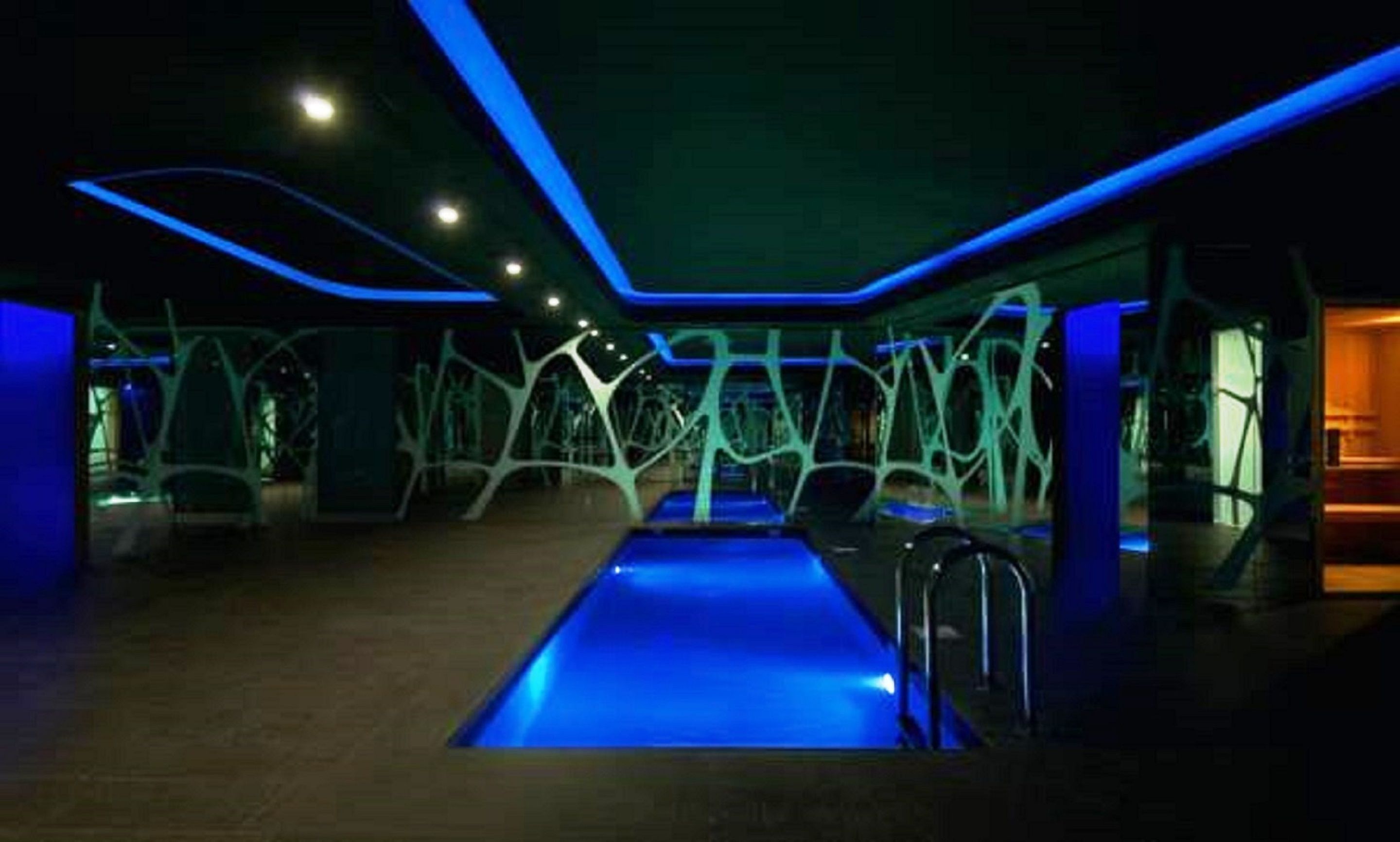 Ein moderner, überdachter Pool mit blauer Beleuchtung und abstrakten Wandgestaltungen.