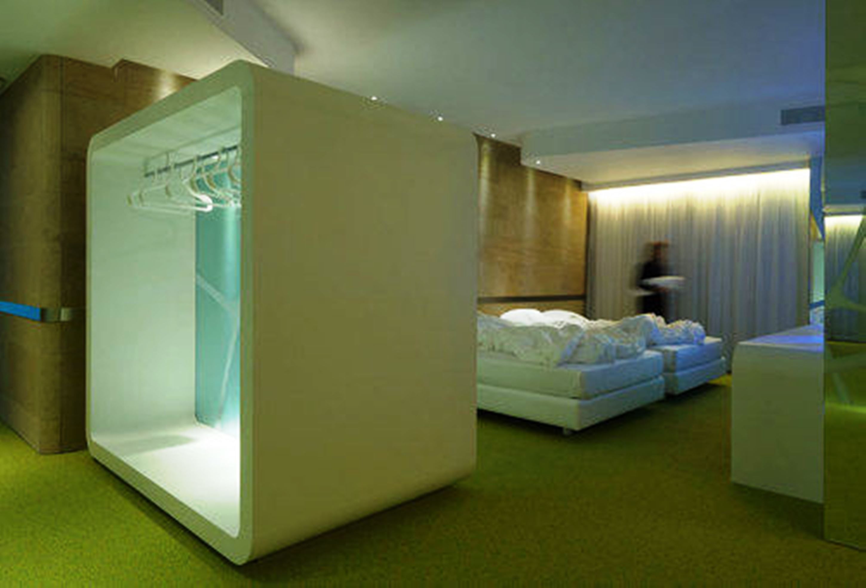 A modern hotel room with a bed, a seating area, and a built-in wardrobe.