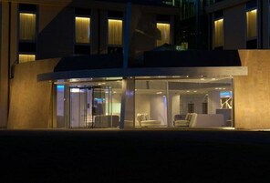 Un hotel moderno con fachada de vidrio, un área de descanso con asientos y una escalera que conduce a un nivel superior.