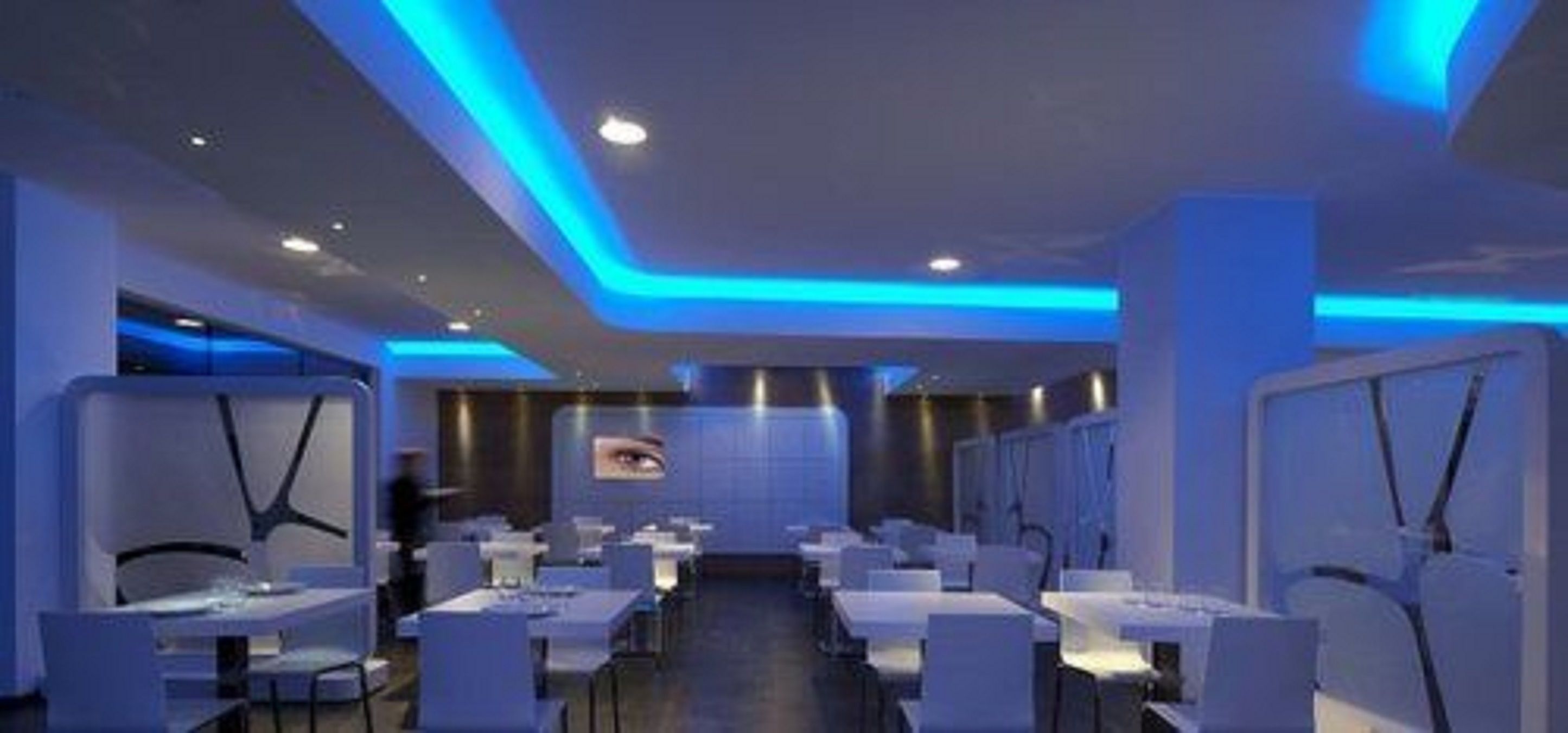 A modern restaurant with a blue-lit ceiling and white tables and chairs.